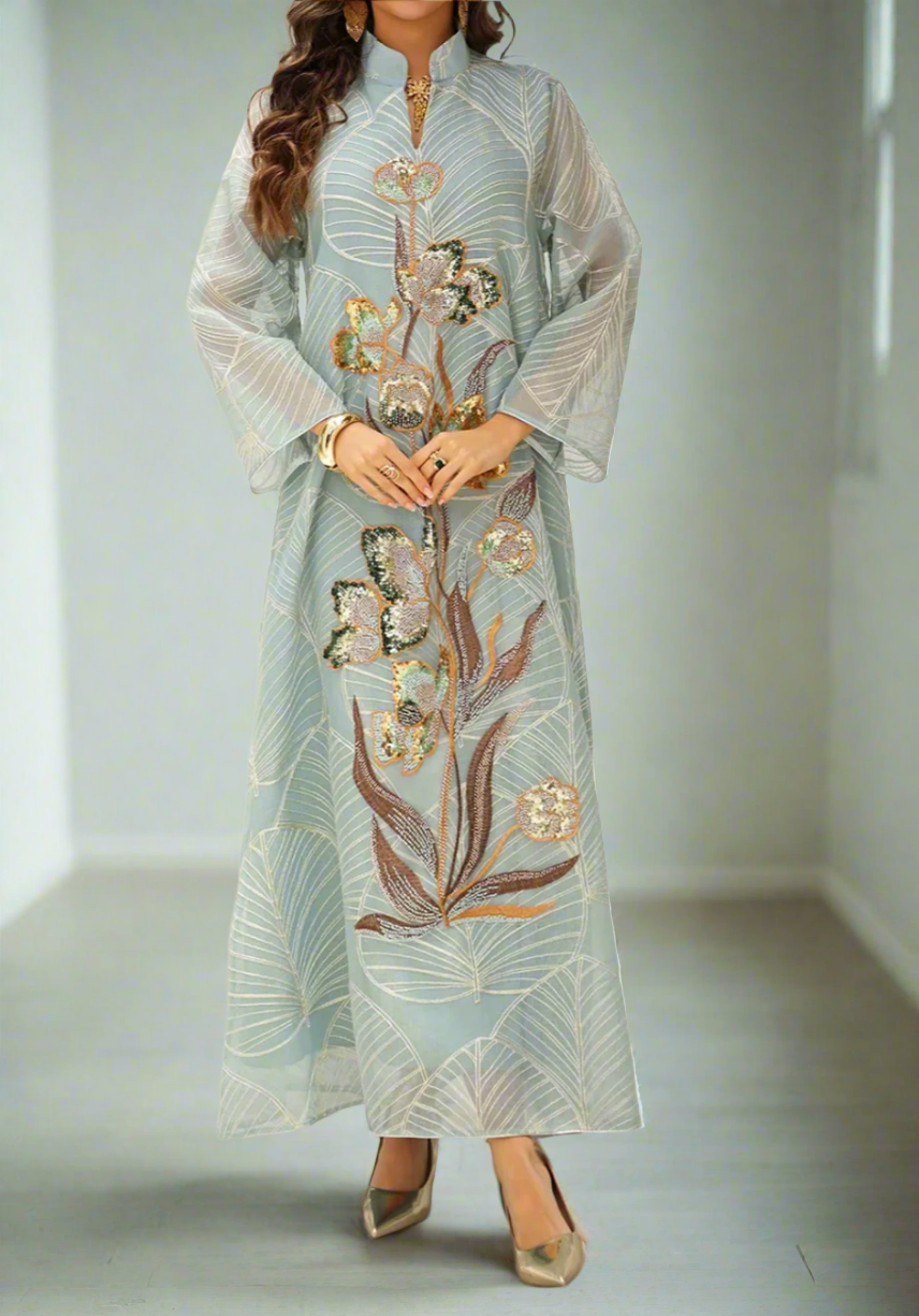 Woman wearing a long, light blue embroidered dress with floral patterns on a neutral background
